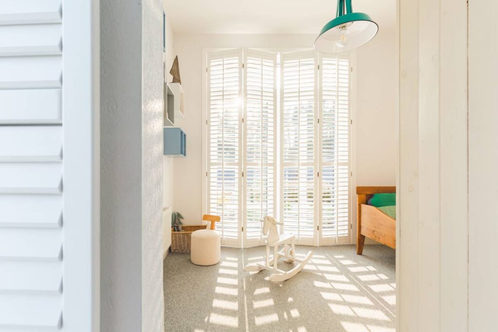 Cute scandinavian style kid's bedroom with floor to ceiling window an rocking horse and plantation shutters