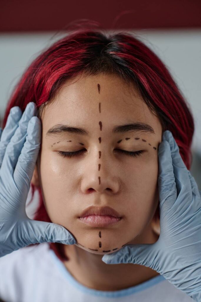 Gloved hands of plastic surgeon touching face of teenage patient with liftmarks while preparing girl for cosmetic procedure