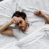 top view of sleeping young man lying under blanket in bed at home